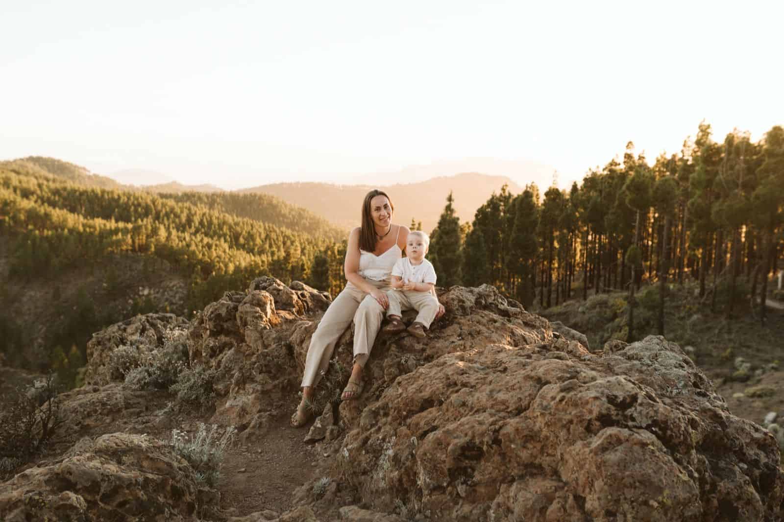 Madre e hijo sentados sonriendo en las montañas de Gran Canaria con un pinar de fondo