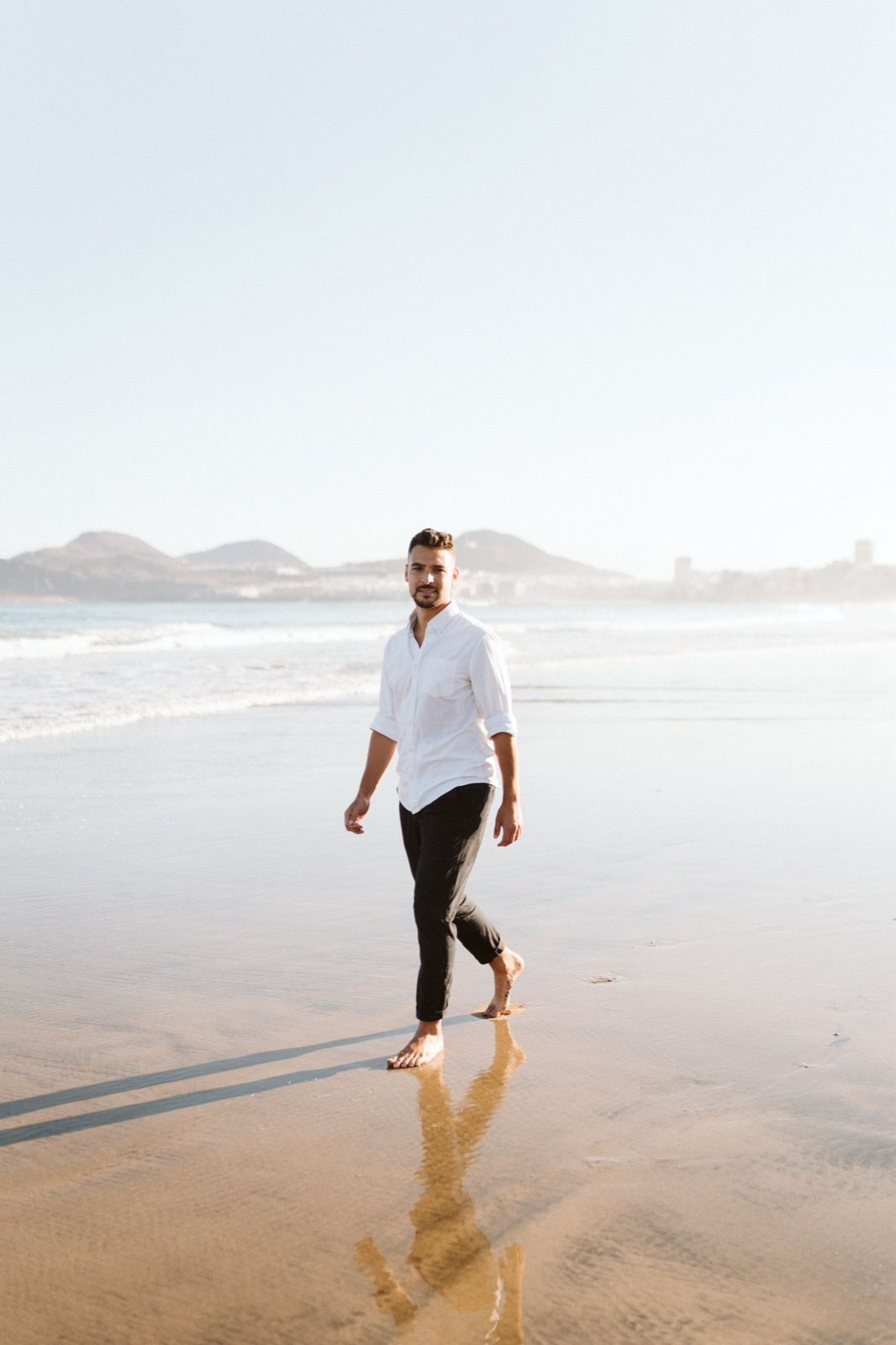 Hombre caminando y posando a la cámara sonriendo en la orilla de la Playa de Las Canteras en Gran Canaria durante las horas de marea baja. Fotografía realizada por el fotógrafo de familias en Gran Canaria Héctor Cardeñosa.