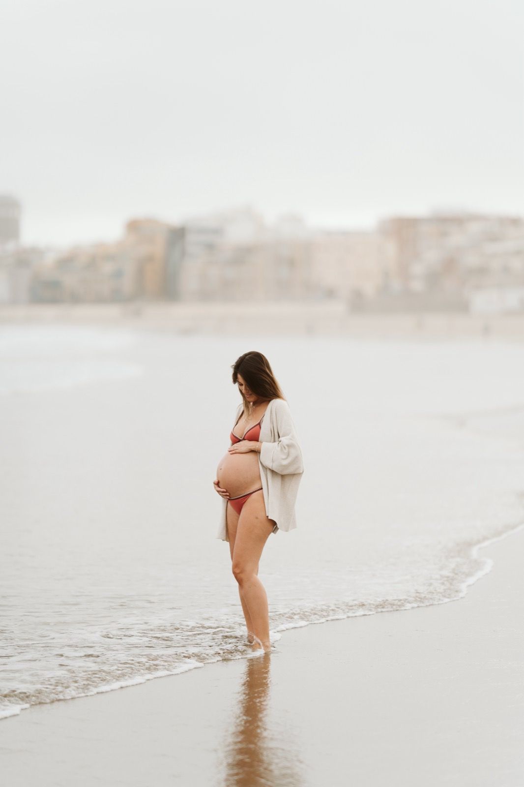 Futura madre abrazando su vientre mientras camina por la orilla de la playa de Las Canteras