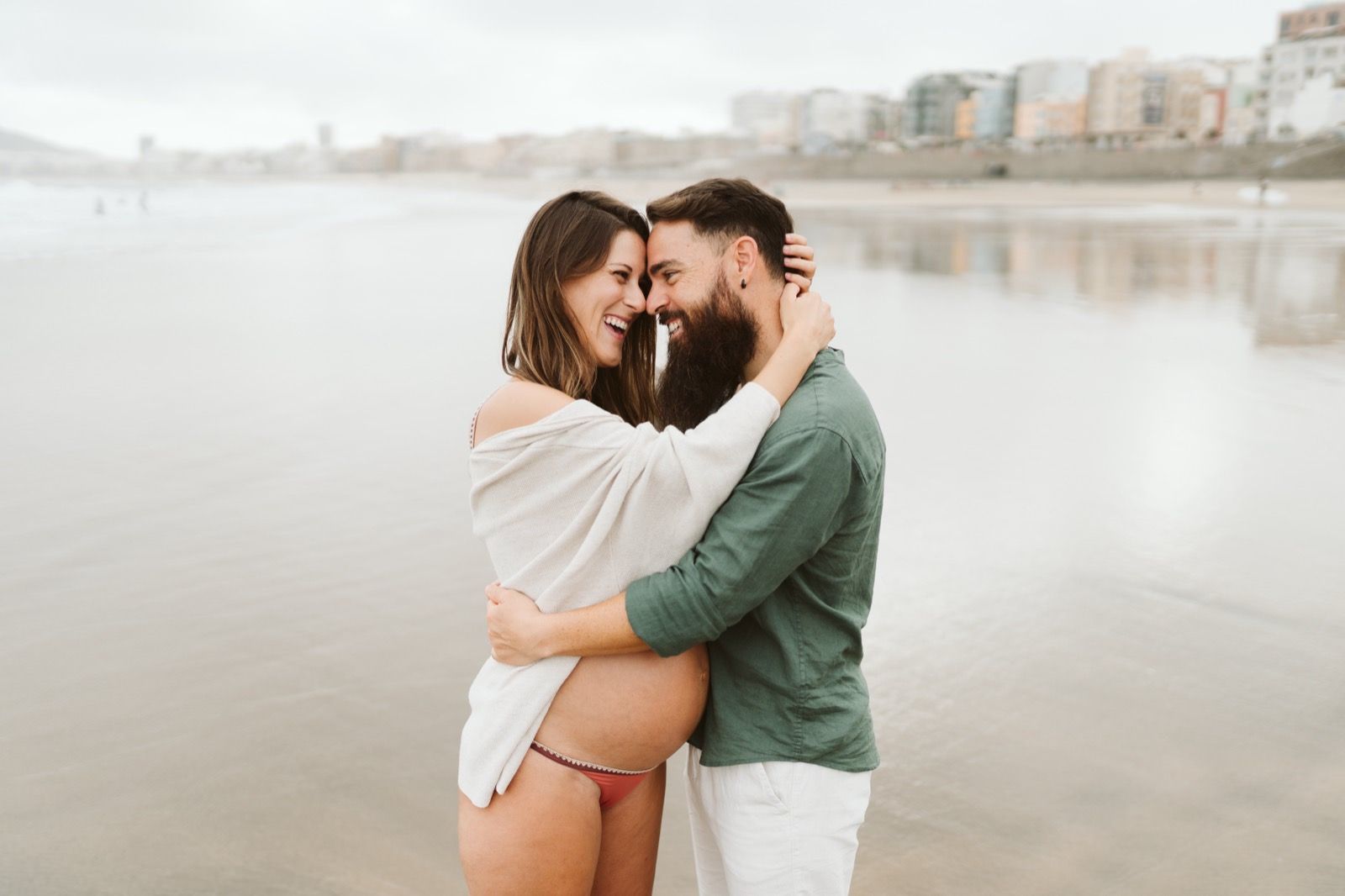 Pareja de novios abrazados disfrutando de una sesión de fotos de embarazo en la playa de Las Canteras, Gran Canaria