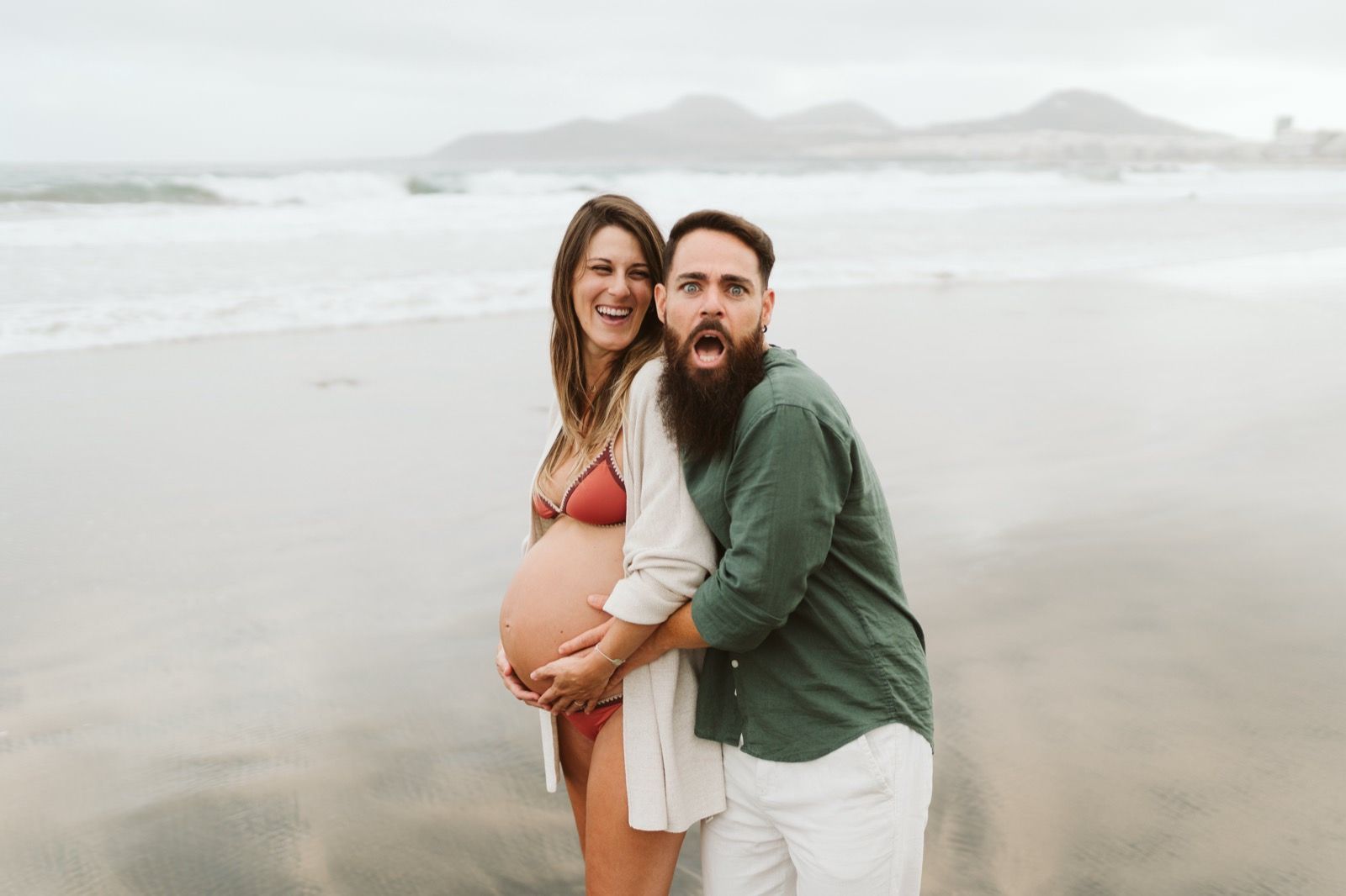Pareja disfrutando de una sesión de fotos de embarazo en la playa de Las Canteras, Gran Canaria, con expresiones divertidas y espontáneas