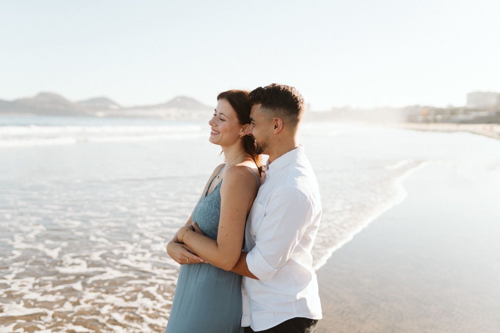 Pareja abrazada a la orilla de la Playa de Las Canteras posando durante la primera hora de la mañana en marea baja. Fotografía realizada por el fotógrafo de familias en Gran Canaria Héctor Cardeñosa.