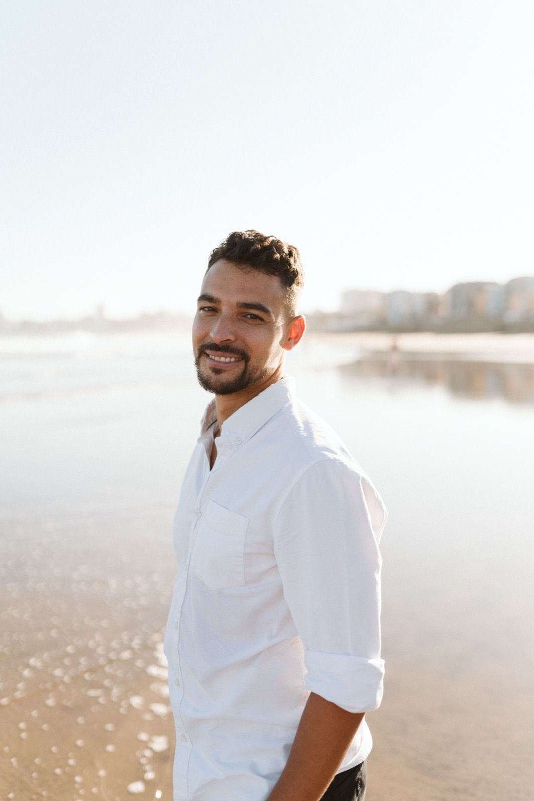 Hombre posando a la cámara sonriendo en la orilla de la Playa de Las Canteras en Gran Canaria durante las horas de marea baja. Fotografía realizada por el fotógrafo de familias en Gran Canaria Héctor Cardeñosa.