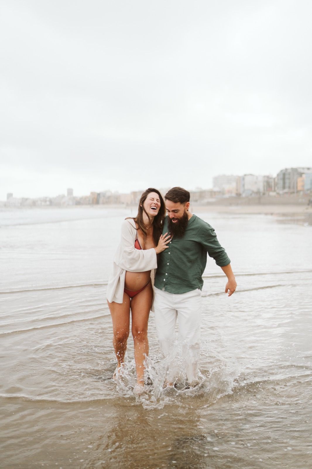 Pareja corriendo por la orilla de la playa durante unas fotos de embarazo en la Playa de Las Canteras