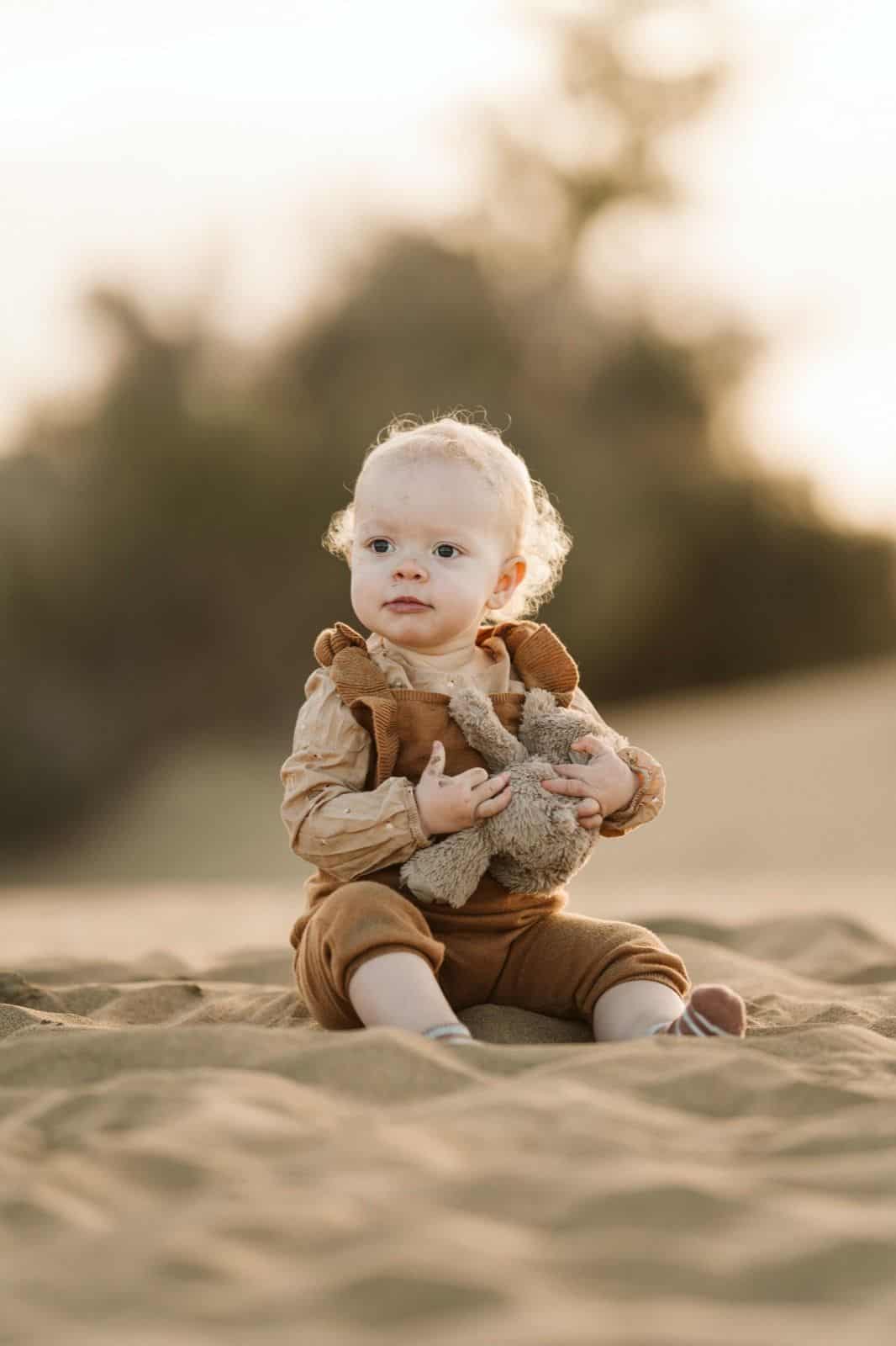 Bebé riendo mientras juega con su peluche en la arena durante una sesión de fotos en las dunas de Maspalomas, Gran Canaria