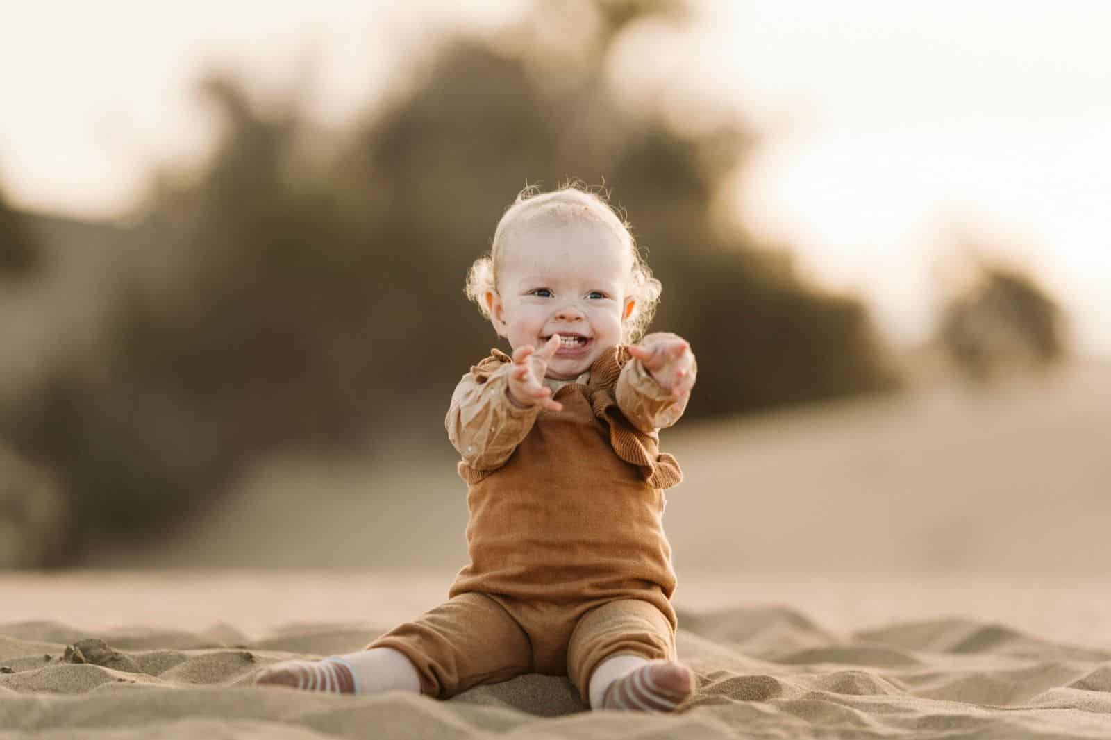 Bebé riendo buscando los brazos de sus padres durante una sesión de fotos en las dunas de Maspalomas, Gran Canaria
