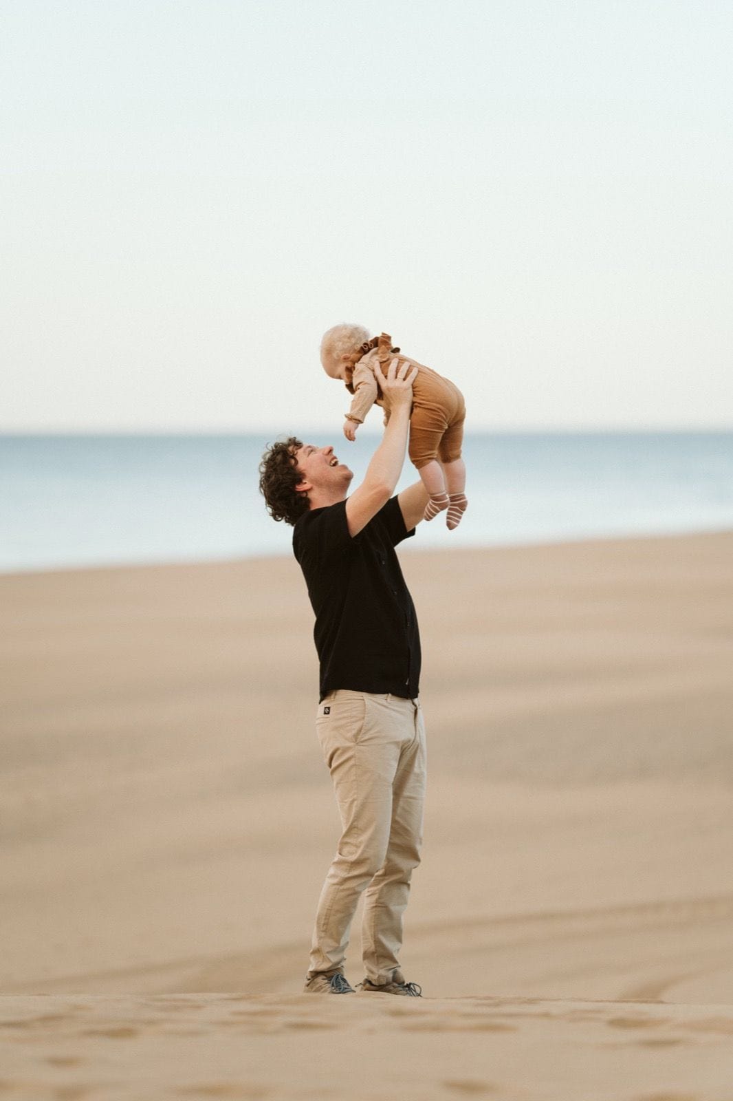 Padre levantando a su bebé sonriente en una sesión de fotos familiares en las dunas de Maspalomas, Gran Canaria