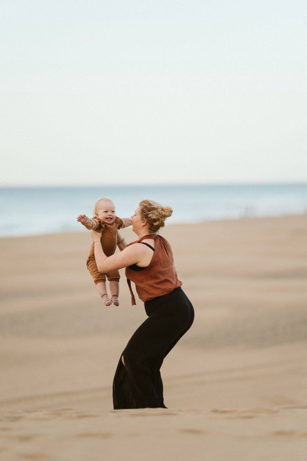 Madre levantando a su bebé sonriente en una sesión de fotos familiares en las dunas de Maspalomas, Gran Canaria